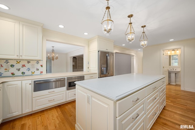 kitchen with an inviting chandelier, light countertops, a warming drawer, stainless steel fridge, and light wood-style flooring