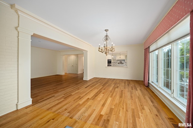 unfurnished dining area featuring ornamental molding, baseboards, a chandelier, light wood-style flooring, and brick wall
