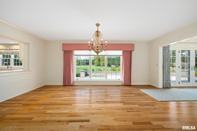 interior space with crown molding, brick wall, light wood finished floors, baseboards, and a notable chandelier