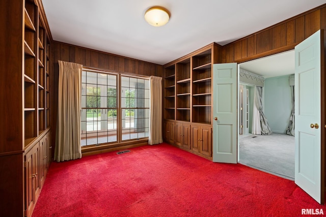 carpeted spare room featuring wooden walls and visible vents