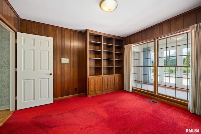unfurnished room featuring wooden walls, carpet, and visible vents