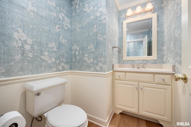 bathroom with toilet, wainscoting, wallpapered walls, wood finished floors, and vanity
