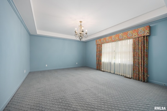 carpeted empty room with baseboards, a tray ceiling, and a chandelier