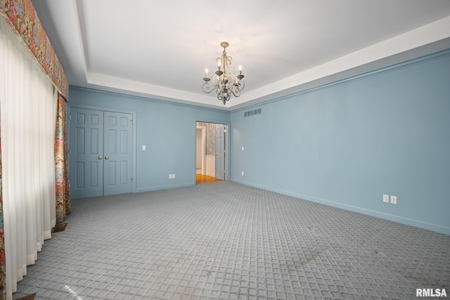 carpeted spare room featuring baseboards, visible vents, a notable chandelier, and a raised ceiling