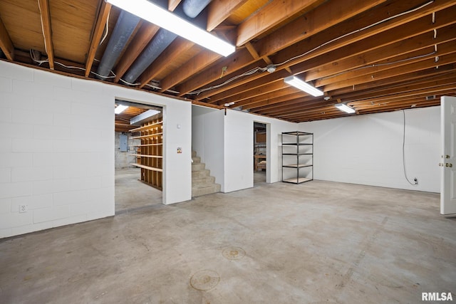 unfinished basement with concrete block wall, stairs, and electric panel