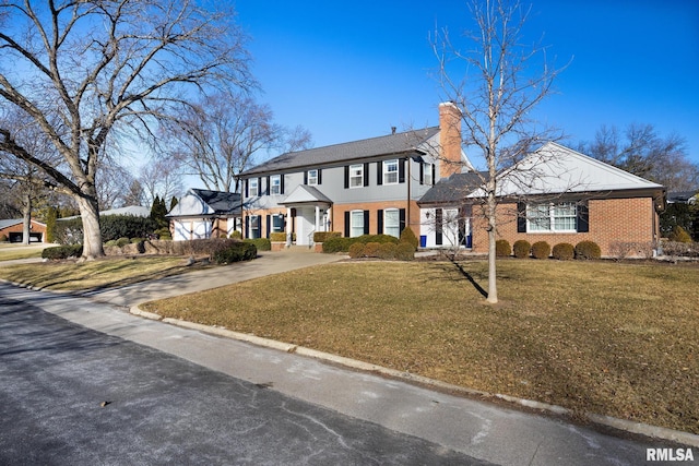 colonial home with a front lawn, driveway, brick siding, and a chimney