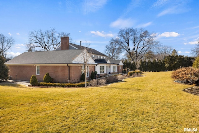 view of side of property with brick siding, a chimney, and a lawn