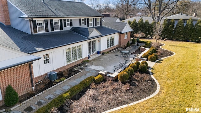 back of property with a lawn, roof with shingles, cooling unit, and a patio