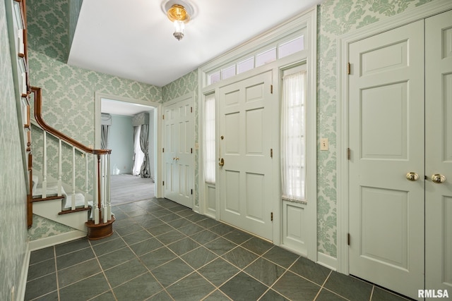 entrance foyer featuring wallpapered walls, baseboards, stairs, and dark tile patterned flooring