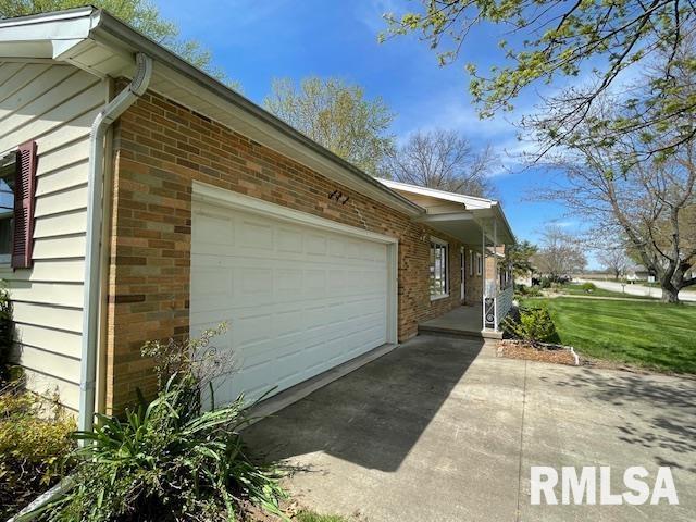 view of home's exterior featuring a garage, brick siding, concrete driveway, and a lawn