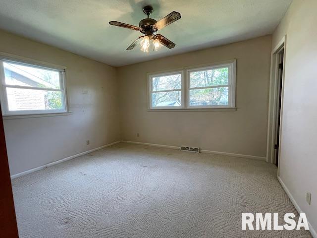 carpeted empty room with a healthy amount of sunlight, baseboards, ceiling fan, and visible vents