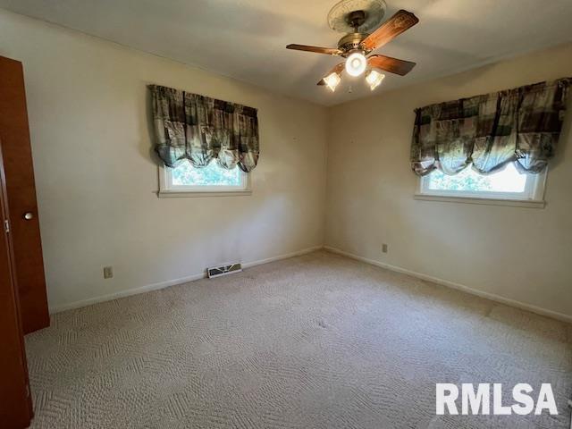 carpeted spare room featuring a wealth of natural light, a ceiling fan, baseboards, and visible vents