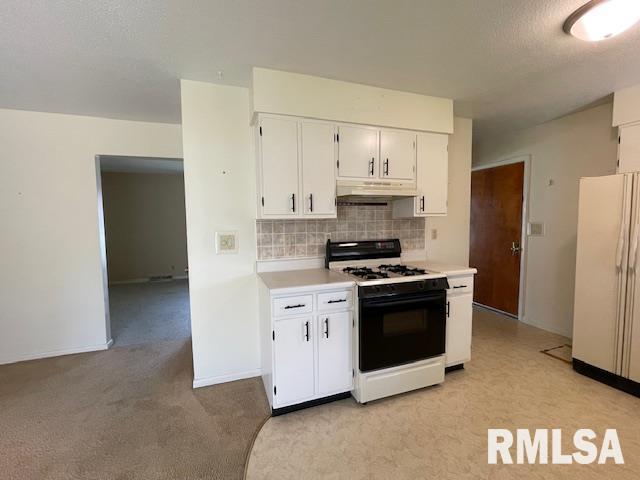 kitchen with tasteful backsplash, light countertops, gas range oven, white cabinets, and freestanding refrigerator
