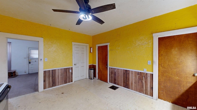 empty room with tile patterned floors, wainscoting, wooden walls, ceiling fan, and a textured wall