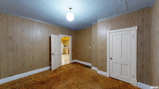 unfurnished room with carpet, visible vents, wood walls, and baseboards