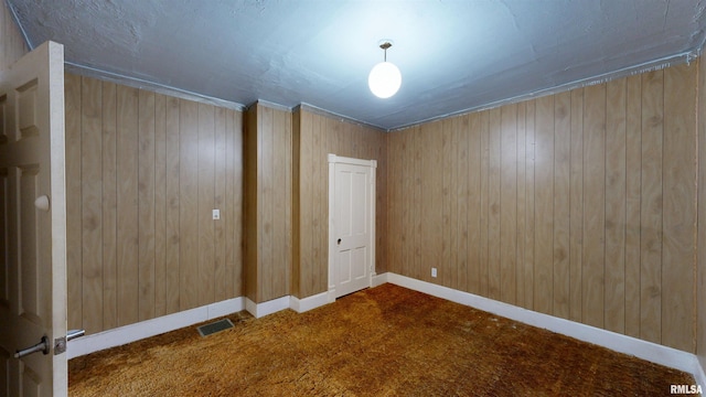 carpeted spare room with visible vents, wood walls, and baseboards