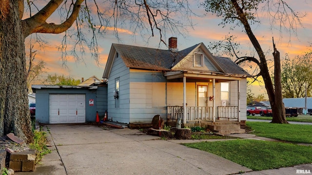 bungalow-style home featuring a chimney, a yard, an attached garage, driveway, and a porch