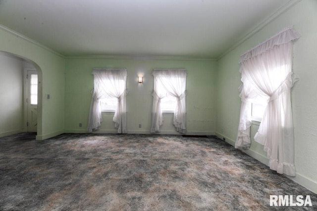 empty room featuring crown molding, arched walkways, carpet flooring, and baseboards