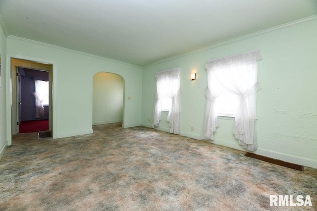 carpeted empty room with crown molding, arched walkways, and baseboards