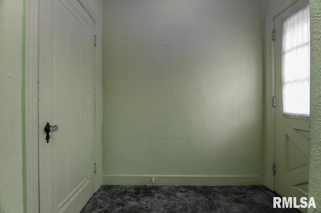 interior space with plenty of natural light, dark carpet, and baseboards