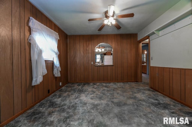 empty room featuring ceiling fan, wood walls, and carpet