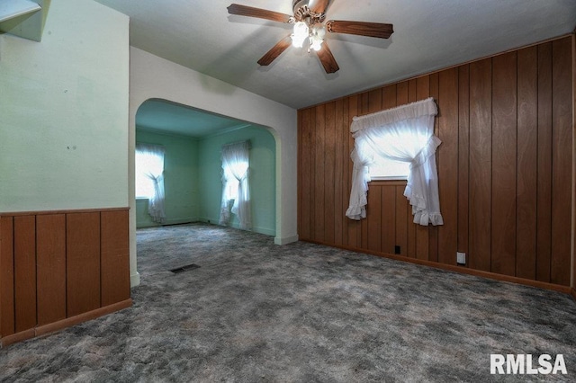 interior space featuring wooden walls, ceiling fan, visible vents, and arched walkways