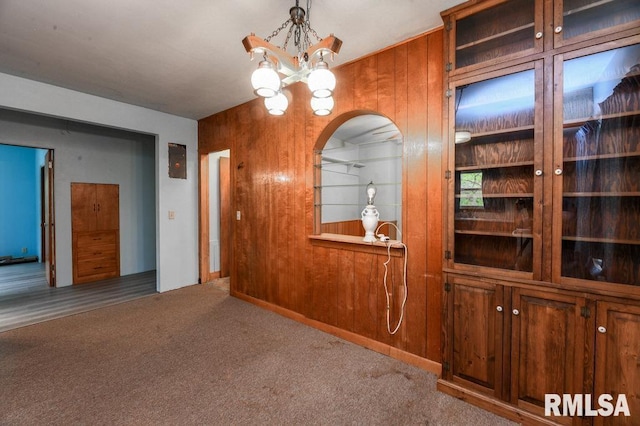 unfurnished dining area featuring wood walls, a chandelier, arched walkways, and carpet floors