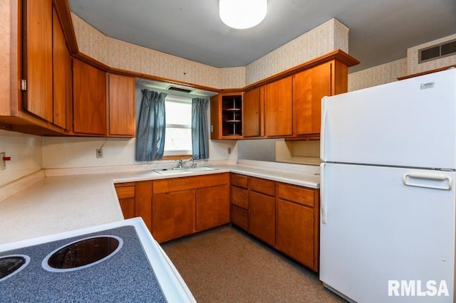 kitchen featuring brown cabinets, light countertops, freestanding refrigerator, and a sink