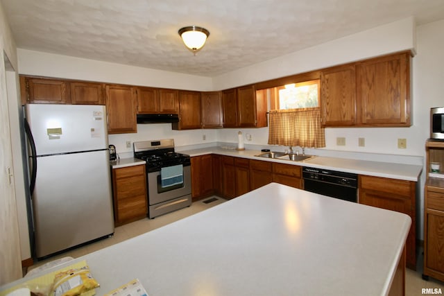 kitchen with brown cabinets, a sink, under cabinet range hood, light countertops, and appliances with stainless steel finishes