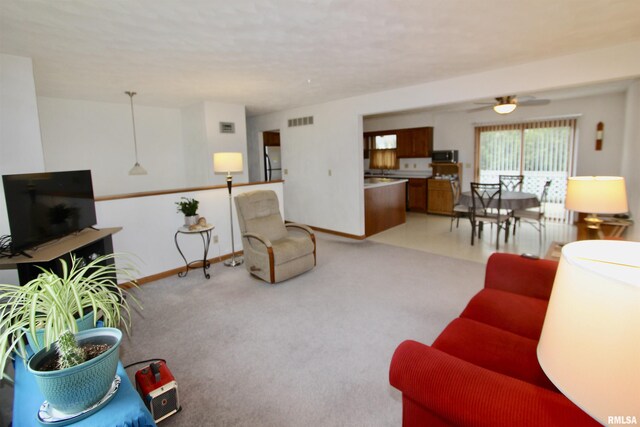 living area with light colored carpet, visible vents, ceiling fan, and baseboards