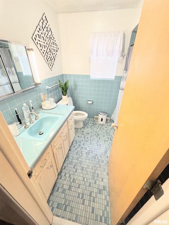 full bath featuring plenty of natural light, tile patterned floors, a wainscoted wall, toilet, and vanity