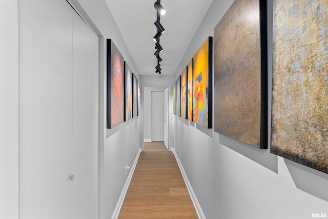corridor with baseboards, light wood finished floors, and rail lighting
