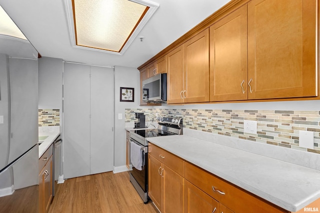 kitchen with brown cabinetry, decorative backsplash, light countertops, light wood finished floors, and appliances with stainless steel finishes