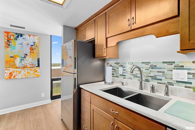 kitchen featuring backsplash, brown cabinets, a sink, freestanding refrigerator, and light wood finished floors