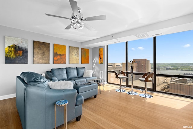 living area featuring wood finished floors, a wall of windows, baseboards, ceiling fan, and a water view