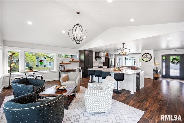 living room featuring an inviting chandelier, vaulted ceiling, wood finished floors, and a wealth of natural light