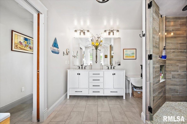 full bath with a sink, baseboards, a tile shower, and double vanity