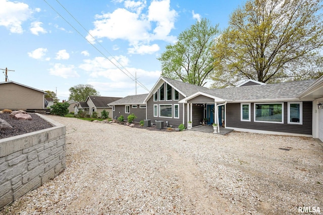 view of front facade featuring roof with shingles, central air condition unit, and gravel driveway