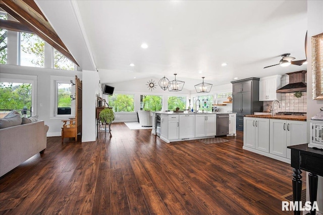kitchen featuring appliances with stainless steel finishes, a sink, open floor plan, wall chimney exhaust hood, and dark wood-type flooring