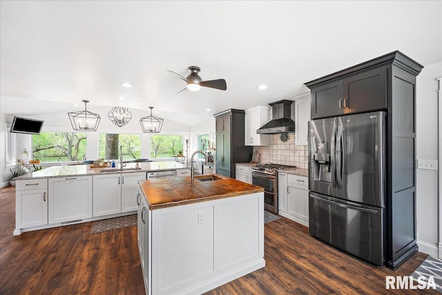 kitchen featuring ceiling fan, appliances with stainless steel finishes, a sink, a kitchen island with sink, and wall chimney exhaust hood