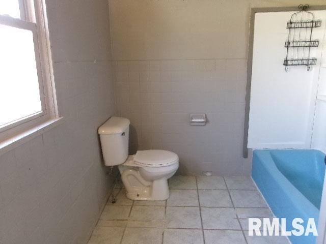 full bath with a wealth of natural light, toilet, a bathing tub, and tile walls