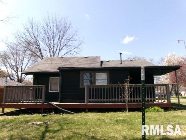 back of property featuring a deck, a yard, and a shingled roof