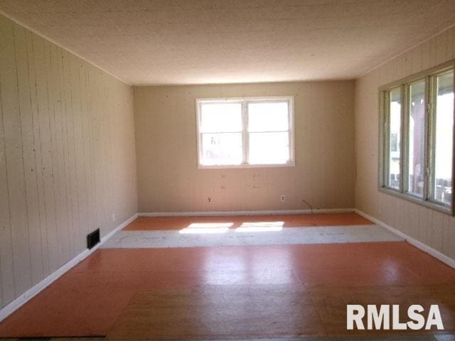 unfurnished room with tile patterned floors, visible vents, and wooden walls