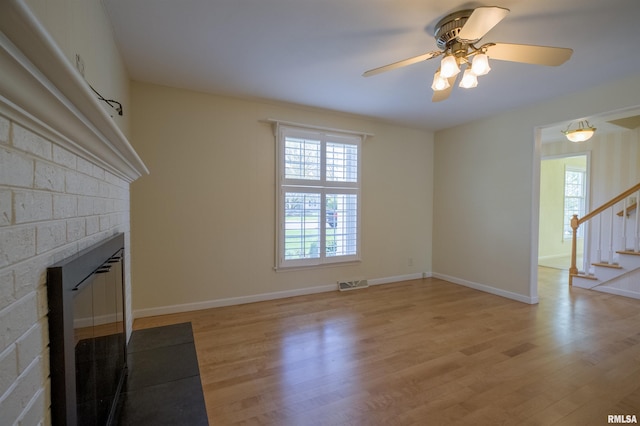 unfurnished living room featuring stairway, ceiling fan, a fireplace, and light wood finished floors