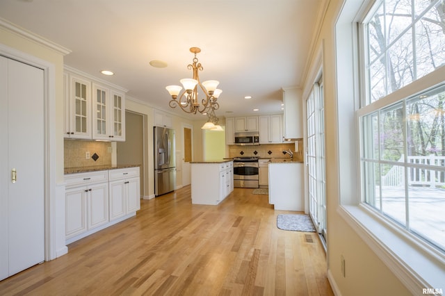 kitchen with decorative backsplash, stainless steel appliances, a kitchen island, light wood finished floors, and a notable chandelier