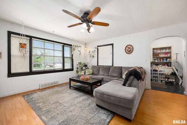 living area with visible vents, baseboards, arched walkways, wood finished floors, and a ceiling fan