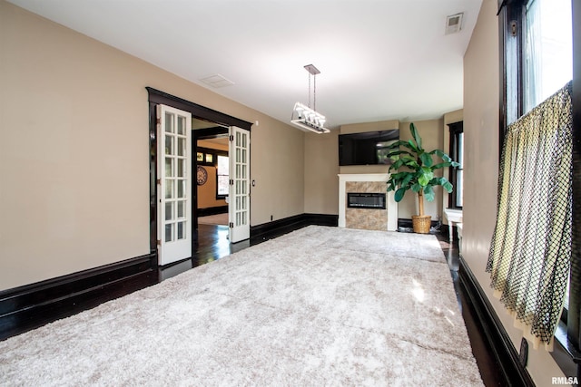 unfurnished living room featuring a premium fireplace, visible vents, baseboards, french doors, and wood finished floors