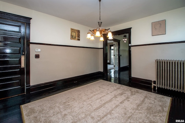 unfurnished room with a chandelier, radiator heating unit, wood finished floors, and baseboards