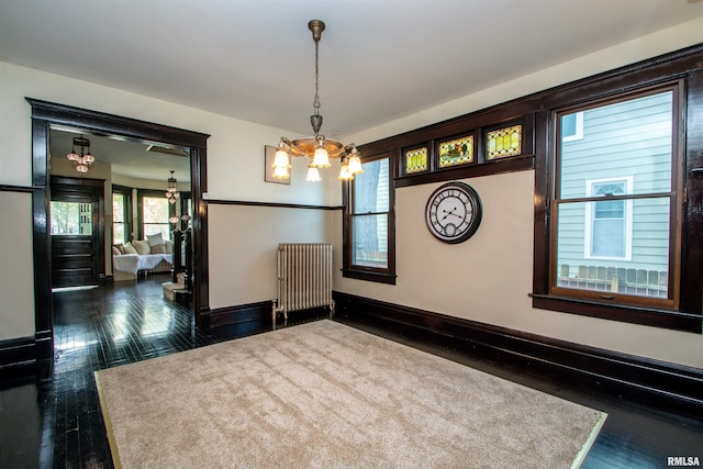 unfurnished dining area featuring radiator, dark wood-style floors, a notable chandelier, and baseboards