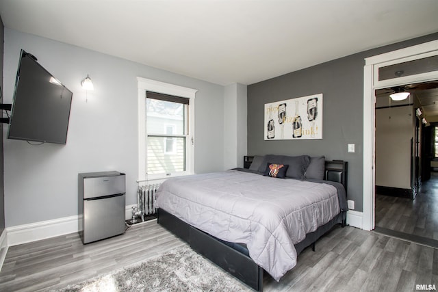 bedroom featuring radiator heating unit, wood finished floors, freestanding refrigerator, and baseboards